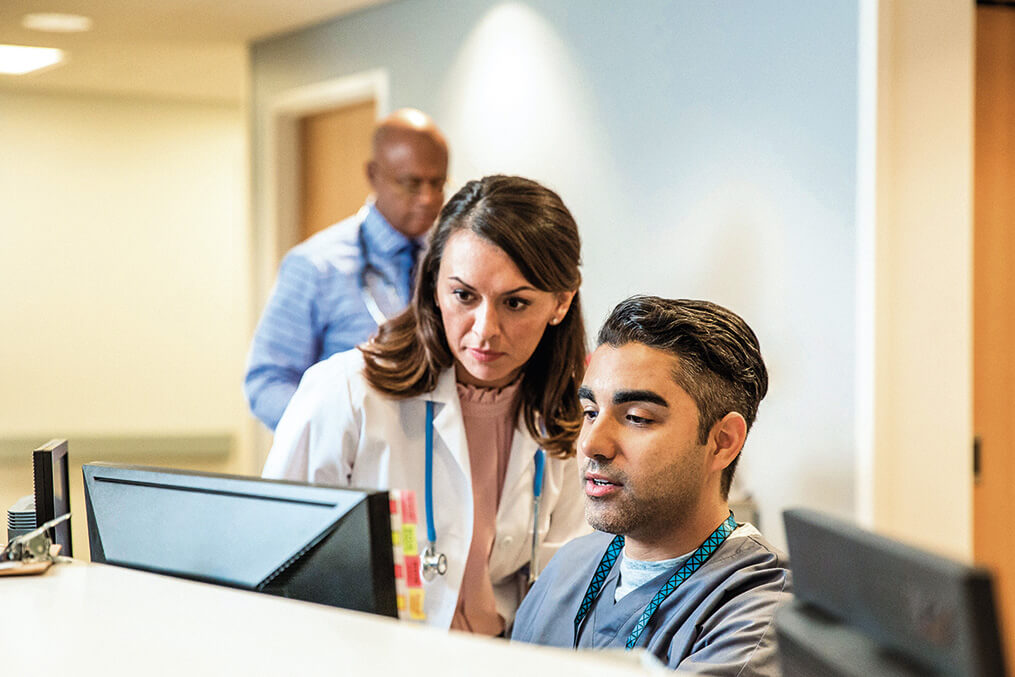 female and male clinician look at computer screen in healthcare setting.