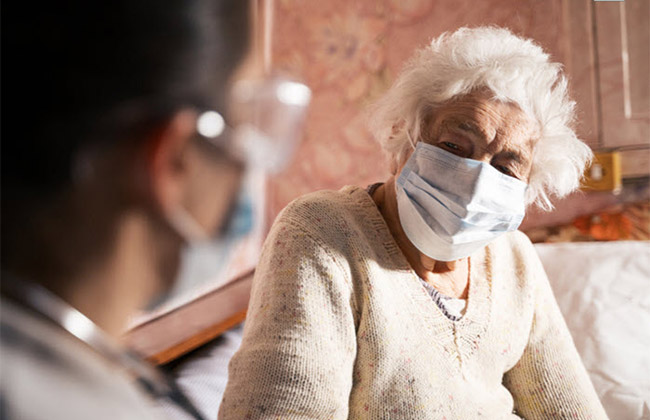 Elderly woman talking to nurse wearing a protective mask.