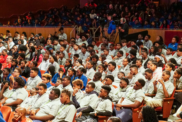 children seated in auditorium listen to presenter