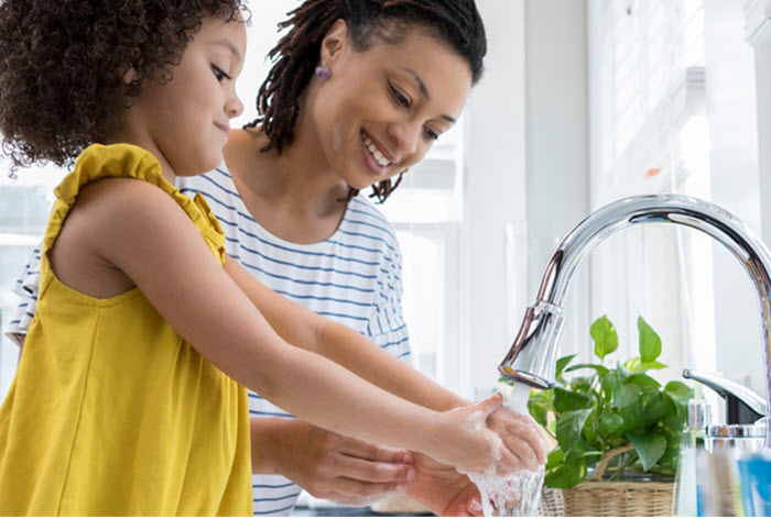 smiling mother and daughter wash hands at sink