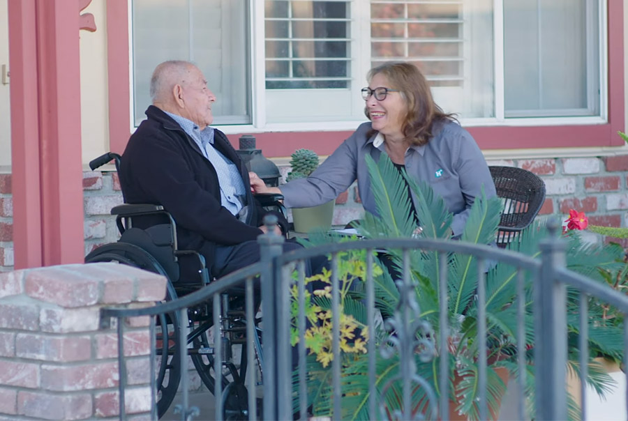 caregiver with an elderly man in wheelchair sitting and laughing on porch