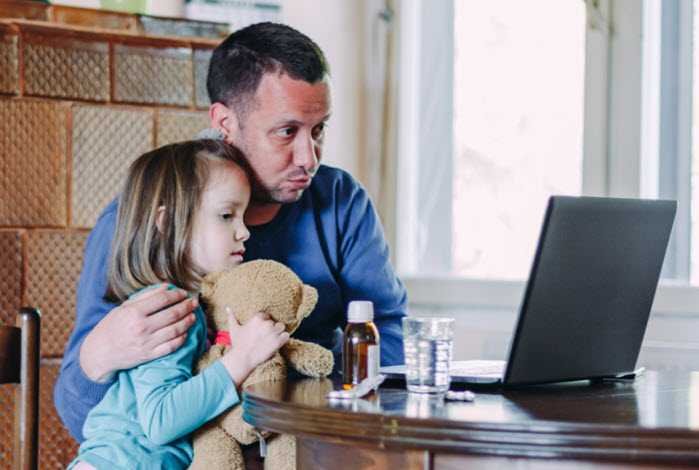 man puts arm around sick child while checking symptoms online