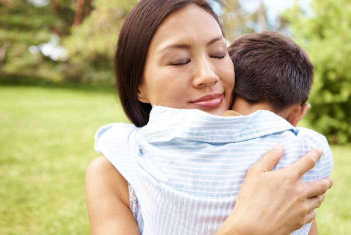 Mom hugging her young son in a park.