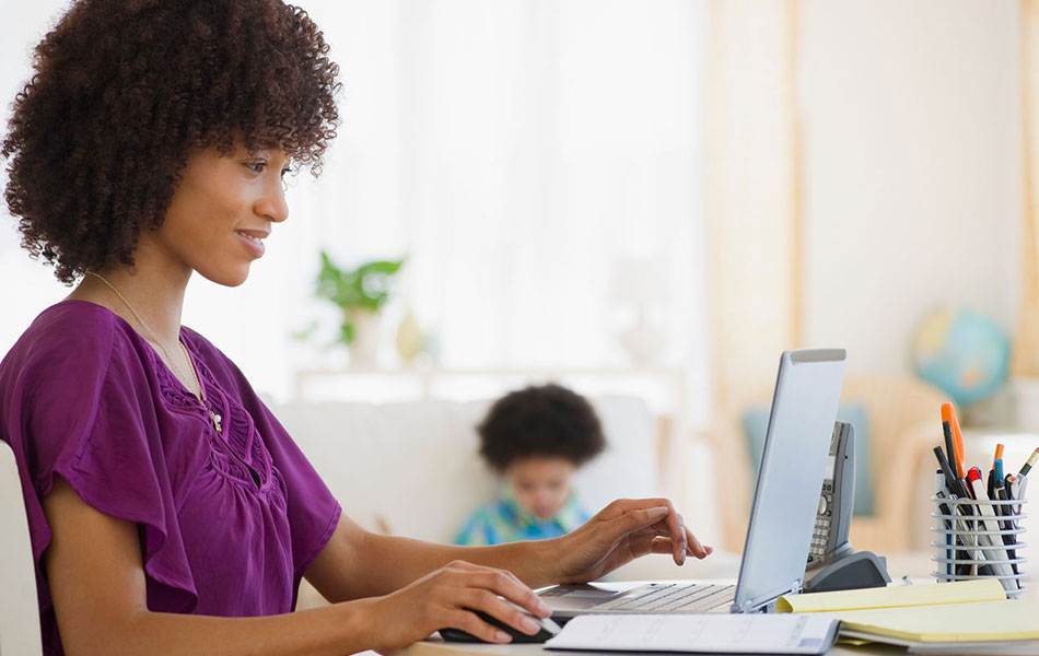 mother typing on laptop with a child in the background