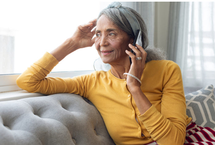 elderly woman talks on phone while sitting on couch