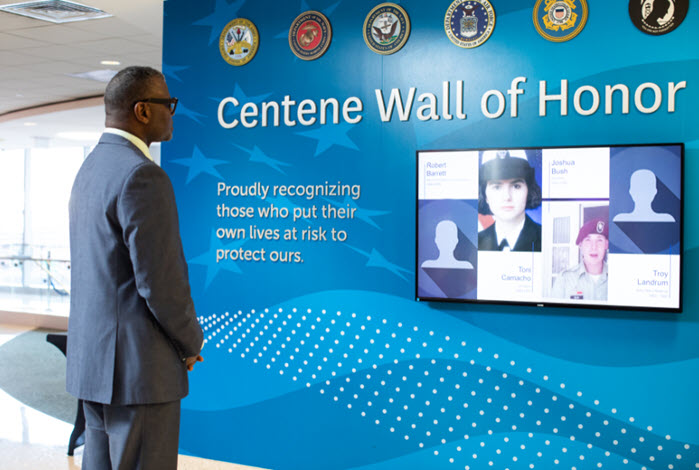 employee standing in front of company wall of honor