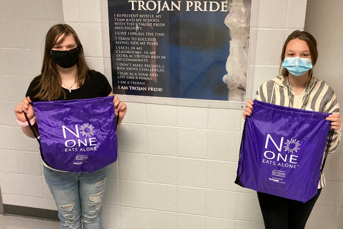 two students hold promotional no one eats alone bags