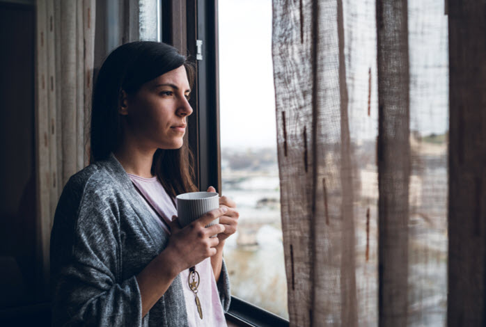 woman looks out window while holding mug