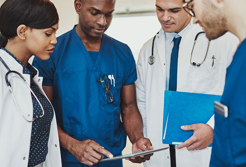 Four physicians in scrubs standing together and looking at a tablet