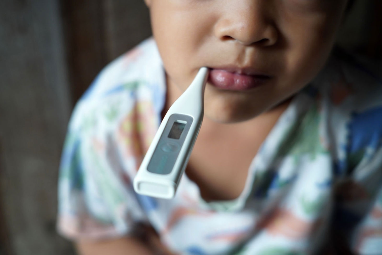child holding an oral thermometer in their mouth