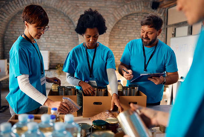 Volunteers in blue shirts pack canned goods and bottled water into boxes at a food donation center